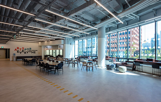 There are chairs and tables in front of a large window with a panoramic view of the lounge.